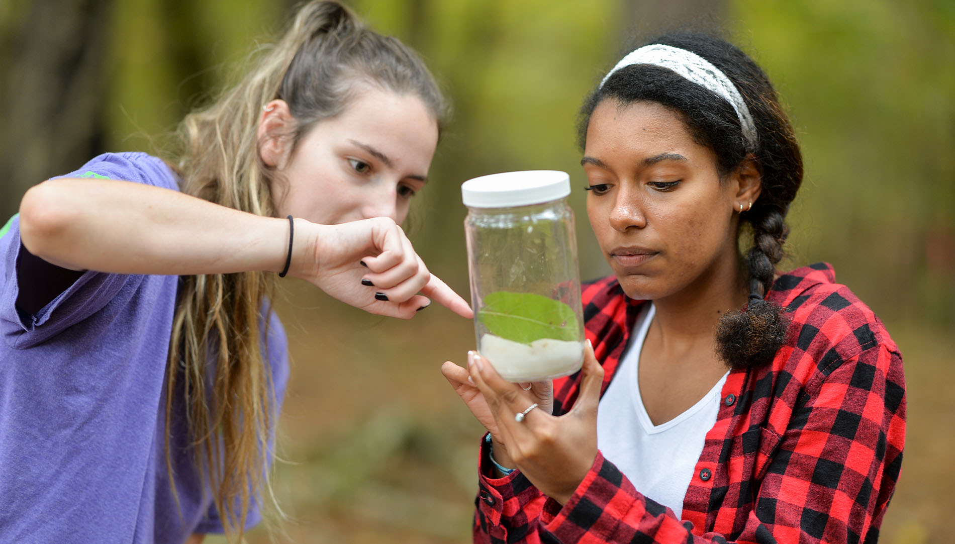 two female students examening plants and specimen in a glass jar
