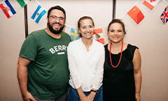 two women and a man smiling in front of assorted flags